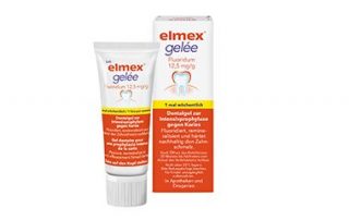 Фотография продукта elmex gelée фторсодержащий зубной гель (12,5 мг/г). На фото изображен белый тюбик и соответствующая складная коробка с оранжево-белым рисунком и символом зуба. Надписи означают профилактику кариеса, реминерализацию зубной эмали и еженедельное применение („1× еженедельно“).